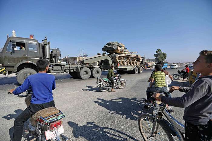 Los habitantes de Maaret al-Numan, en la provincia siria septentrional de Idlib, observan cómo un vehículo transporta un tanque turco que, según se informa, forma parte de un convoy de vehículos militares que se dirige hacia la ciudad de Khan Sheikhoun