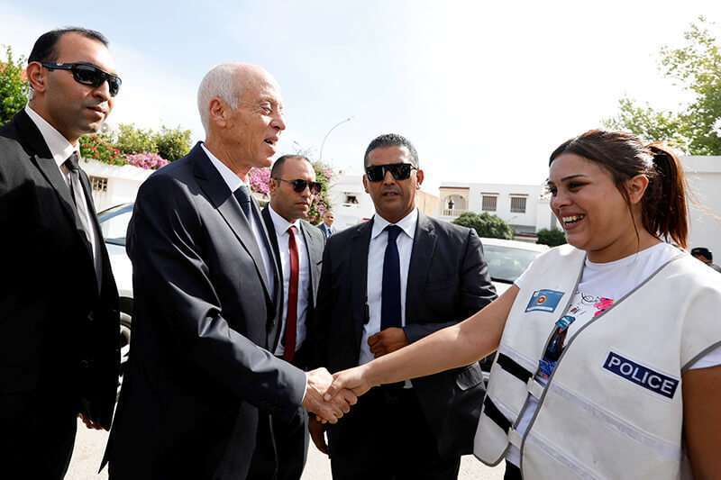 El candidato presidencial tunecino Kais Saied da la mano a un miembro de la policía en una mesa electoral durante la segunda vuelta de las elecciones presidenciales en Túnez, el 13 de octubre de 2019