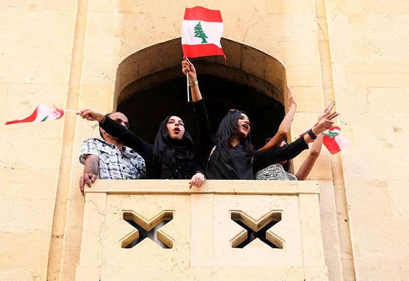 Mujeres enarbolan banderas libanesas en un balcón durante una protesta contra el gobierno por una crisis económica, en Beirut, el 19 de octubre de 2019