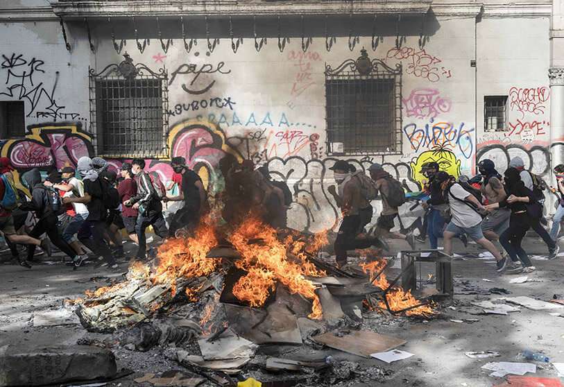 Manifestantes entre los escombros quemados en Plaza Italia durante el quinto día consecutivo de protesta que estalló a causa de un aumento suspendido de los precios de los boletos del metro, en Santiago, el 22 de octubre de 2019.