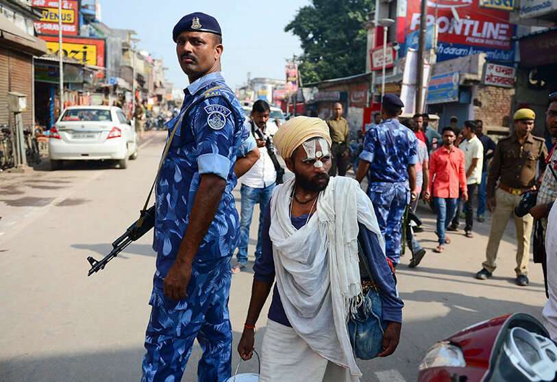 Un hombre hindú pasa por delante de personal de seguridad en una carretera de Ayodhya el 9 de noviembre de 2019, antes de que el Tribunal Supremo dicte sentencia sobre el lugar religioso en disputa. - India se preparó el 9 de noviembre para un fallo de la Corte Suprema sobre un lugar sagrado disputado durante siglos por hindúes y musulmanes, que en 1992 desencadenó algunos de los actos de violencia sectaria más mortíferos desde la independencia