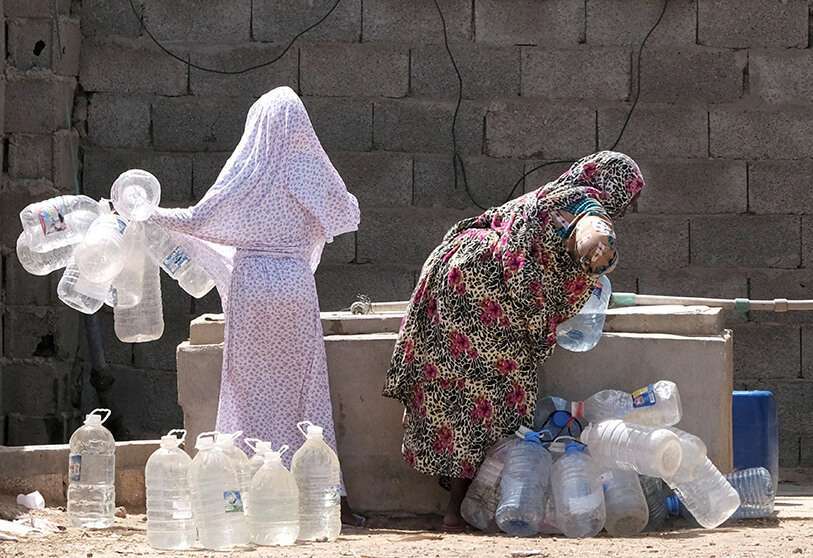 Una mujer libia desplazada de la ciudad de Tawergha llena contenedores con agua en un campamento de desplazados en Bengasi, Libia, el 19 de junio de 2019