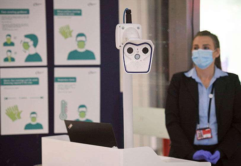 Un miembro del personal se encuentra con un dispositivo de control de la temperatura corporal en la entrada del control de pasaportes en la Terminal 1 del aeropuerto de Manchester, Inglaterra