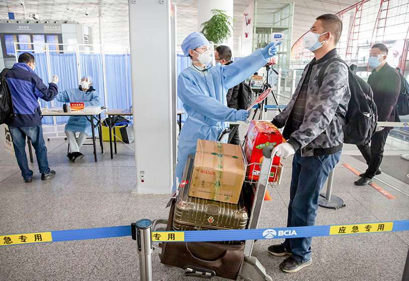 Un trabajador con traje protector toma la temperatura de un viajero en el Aeropuerto Internacional de la Capital de Pekín, el 6 de marzo de 2020