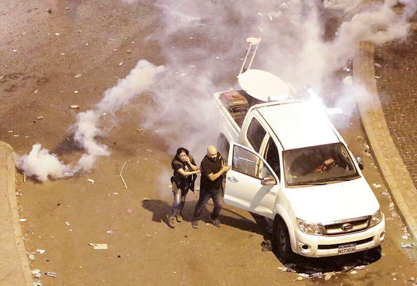 En esta foto del viernes 18 de octubre de 2019, la reportera libanesa Joyce Akiki, izquierda, huye de los gases lacrimógenos durante una protesta antigubernamental, en Beirut, Líbano