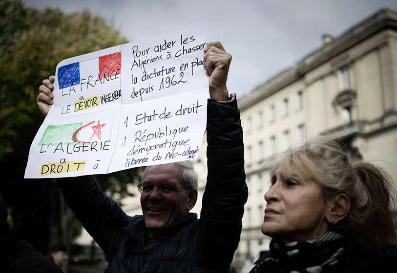 Un manifestante muestra una pancarta durante una protesta contra la represión política en Argelia, cerca de la Asamblea Nacional en París, el 24 de octubre de 2019. - La leyenda de la pancarta dice: "Es deber de Francia ejercer influencia para ayudar a los argelinos a deshacerse de la dictadura que existe desde 1962" (arriba) y "Argelia tiene derecho a ser un Estado de derecho y una república democrática liberada del neocolonialismo"