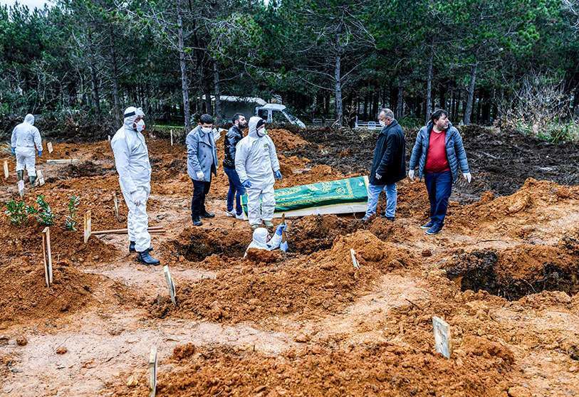 Sanitarios se preparan para enterrar a una persona que murió por el coronavirus, mientras se cavan otras nuevas tumbas en un cementerio abierto para las víctimas de la pandemia
