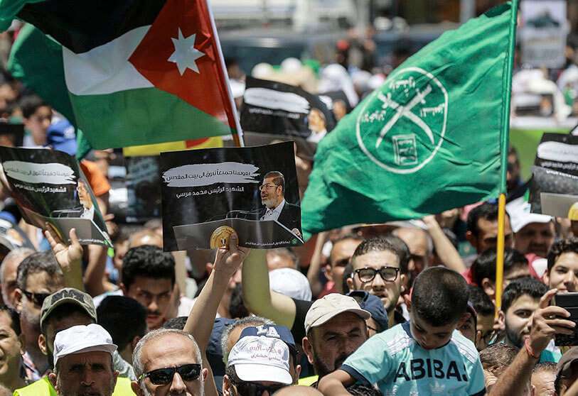La bandera de Jordania (izquierda) y la Hermandad Musulmana (derecha) ondean junto a un cartel que muestra al difunto presidente egipcio Mohamed Morsi, con leyendas en árabe que dicen "nuestras almas anhelan Jerusalén, el mártir Mohamed Morsi", durante una manifestación de oración posterior al viernes en la capital jordana, Amman, el 21 de junio de 2019, contra el "Acuerdo del siglo" del presidente estadounidense Donald Trump