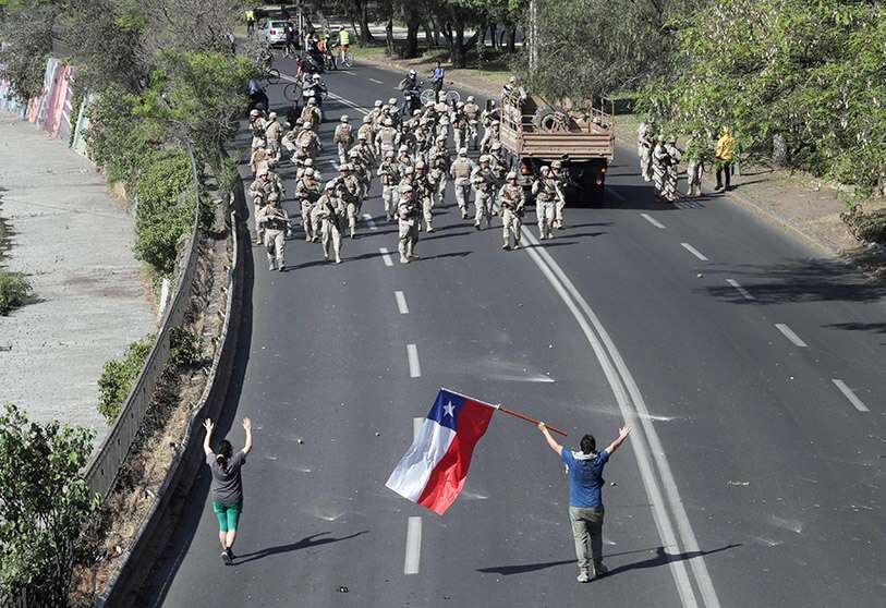 Soldados chilenos se reúnen cerca de manifestantes, uno de los cuales tiene una bandera chilena, durante las protestas contra el Gobierno de Chile en Santiago de Chile, el 20 de octubre de 2019