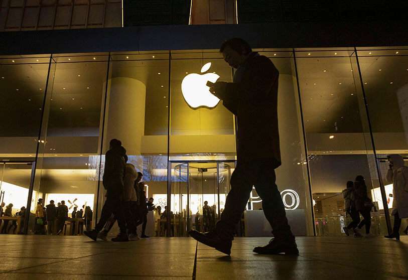 Un hombre mira su teléfono mientras pasa por delante de una tienda del gigante de la tecnología estadounidense Apple en un distrito comercial de Pekín el viernes 13 de diciembre de 2019