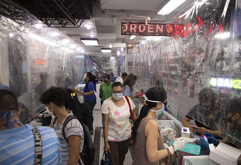 Los compradores que usan máscaras protectoras como medida para ayudar a frenar la propagación del nuevo coronavirus, llenan una tienda de tecnología de teléfonos celulares equipada con láminas de plástico que sirven como cortinas protectoras, en Caracas, Venezuela, el viernes 5 de junio de 2020