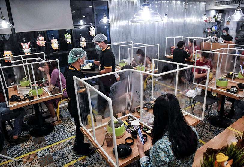 Les gens mangent entre des cloisons en plastique, établies dans le but de contenir toute propagation du coronavirus, au restaurant Penguin Eat Shabu Hotpot à Bangkok, le 5 mai 2020