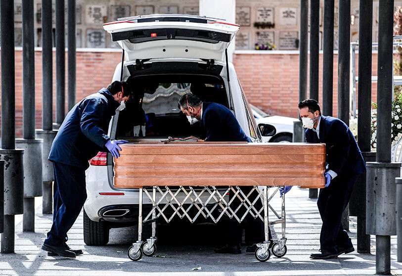 Empleados de la funeraria con máscaras faciales llevan un ataúd al crematorio del cementerio de La Almudena en Madrid, el 24 de marzo de 2020, durante el funeral de una víctima del coronavirus
