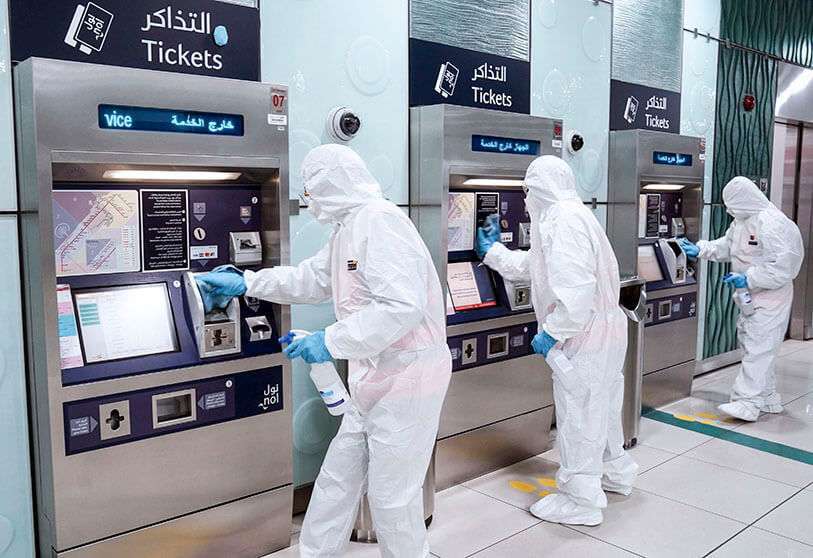 Miembros de un equipo médico rocían desinfectantes en las máquinas expendedoras de billetes, después de que se impusiera un toque de queda para evitar la propagación de la COVID-19 en Dubái