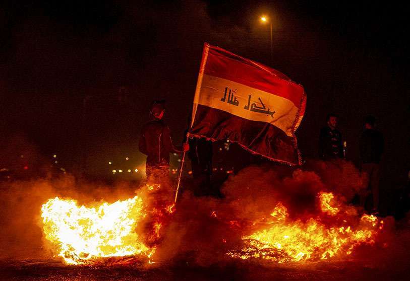 Un manifestante antigubernamental iraquí sostiene una bandera nacional mientras está de pie junto al fuego en un improvisado bloqueo de carretera en la ciudad sureña de Basora a finales del 25 de diciembre de 2019