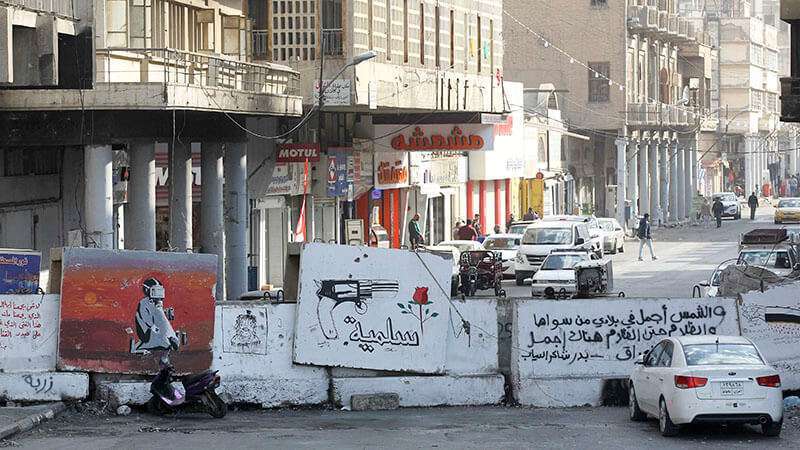 Una vista de una barrera de hormigón a lo largo de la calle Rasheed en la capital iraquí, Bagdad, con un mural de graffiti que representa un arma ante una flor y un texto en árabe que dice “pacífico”, el 25 de diciembre de 2019