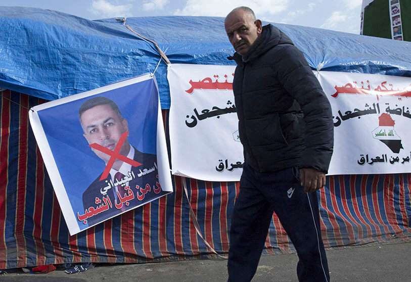 Un manifestante pasa por delante de un cartel con una imagen desfigurada del gobernador de la provincia sureña de Basora, Asaad al-Eidani, en árabe que dice “rechazado por el pueblo”, en la plaza Tahrir, en Bagdad, Irak, el miércoles 25 de diciembre de 2019