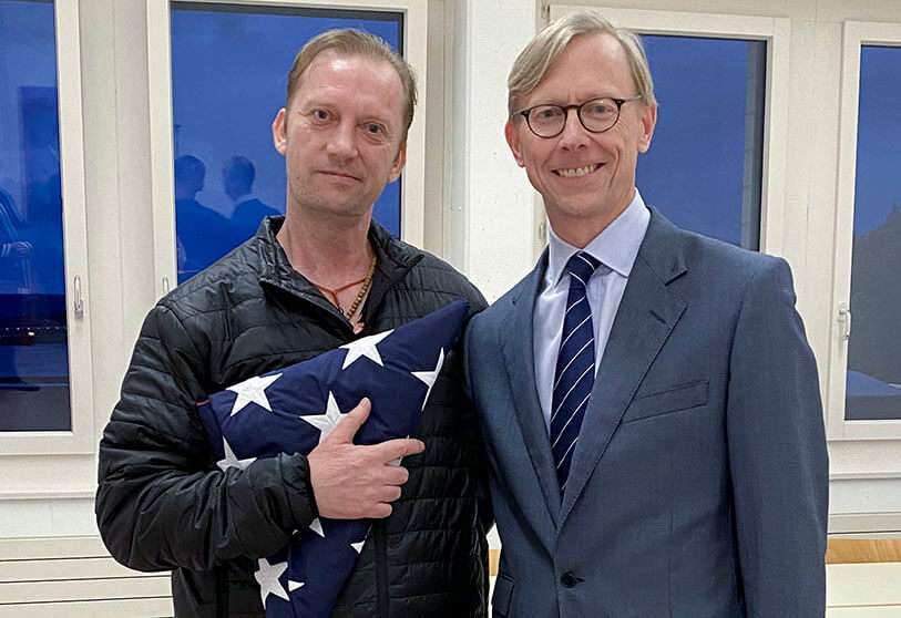 El veterano de la Marina de EEUU Michael White sosteniendo una bandera doblada de los EE.UU. mientras posa con el Enviado Especial de los EE.UU. a Irán Brian Hook en el aeropuerto de Zurich