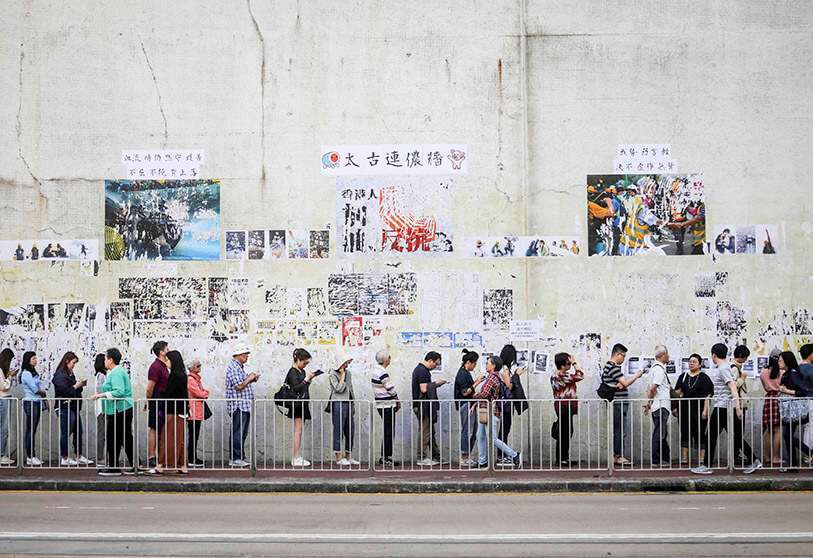 La gente hace cola para emitir su voto frente a un ‘Muro de Lennon’ adornado con carteles destrozados en apoyo de las protestas en curso, durante las elecciones del Consejo de Distrito en Tai Koo, Hong Kong, el 24 de noviembre de 2019
