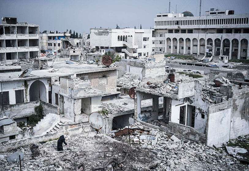 En esta foto del jueves 12 de marzo de 2020, una mujer está de pie en la cima de un edificio en un barrio muy dañado por los ataques aéreos en Idlib, Siria