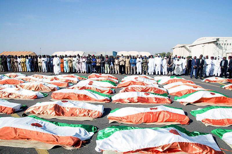 Familias y funcionarios rezan frente a los soldados envueltos en banderas, muertos durante un ataque al campamento del Ejército en la frontera entre Níger y Mali, durante su ceremonia de entierro en el aeropuerto militar de Niamey, Níger, el 13 de diciembre de 2019