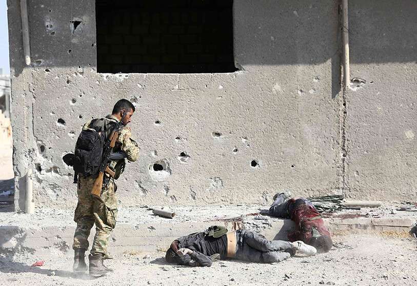 Un combatiente sirio apoyado por Turquía se para sobre cadáveres en la ciudad fronteriza siria de Ras al-Ain el 17 de octubre de 2019