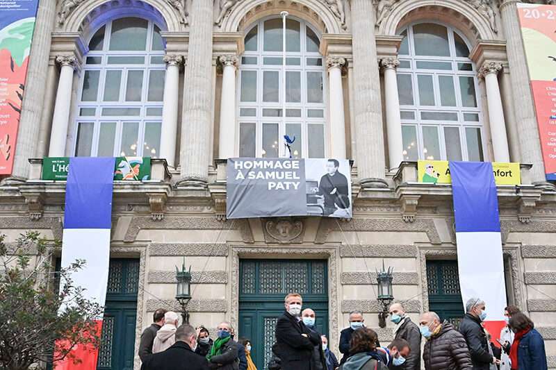 La gente está de pie frente a un retrato del profesor francés Samuel Paty expuesto en la fachada de la Ópera Comedia en Montpellier, el 21 de octubre de 2020