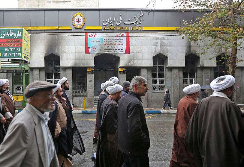 Los iraníes pasan por delante de la sucursal de un banco local que fue dañada durante las manifestaciones contra la subida del precio de la gasolina, el 20 de noviembre de 2019 en Shahriar, al oeste de Teherán AFP/ ATTA KENARE