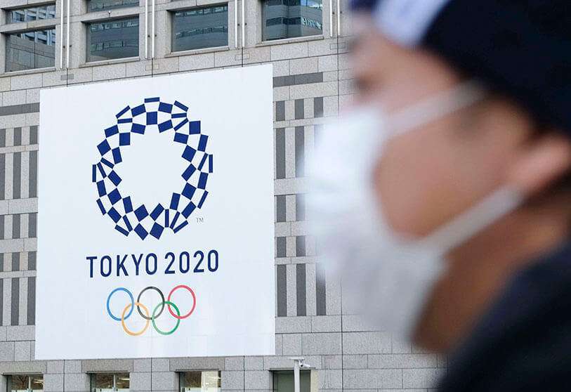 Un hombre con una máscara pasa el logo de los Juegos Olímpicos de Tokio 2020 expuesto en el edificio del Gobierno Metropolitano de Tokio el 19 de marzo de 2020