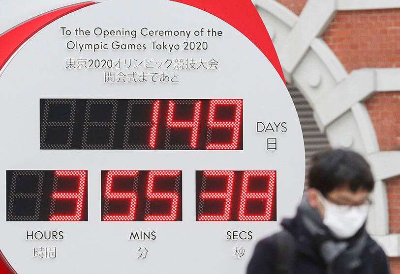 Un hombre lleva una máscara quirúrgica mientras pasa por delante de un gran reloj Omega de cuenta atrás de un año para la ceremonia de apertura de los Juegos Olímpicos y Paralímpicos de Tokio 2020
