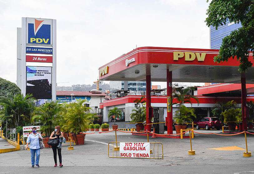 La gente pasa por delante de una gasolinera con un cartel que dice "No hay gasolina"