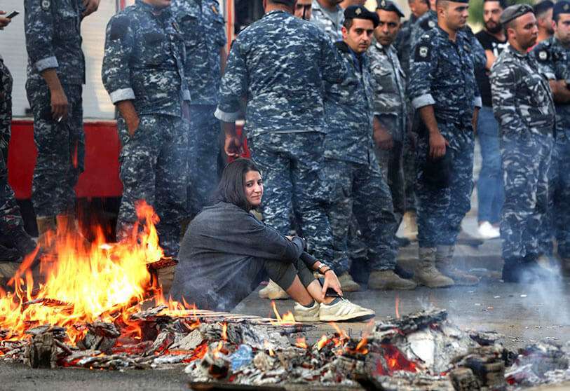 Una manifestante antigubernamental libanesa se sienta en el suelo junto a una barricada en llamas, el 13 de noviembre de 2019