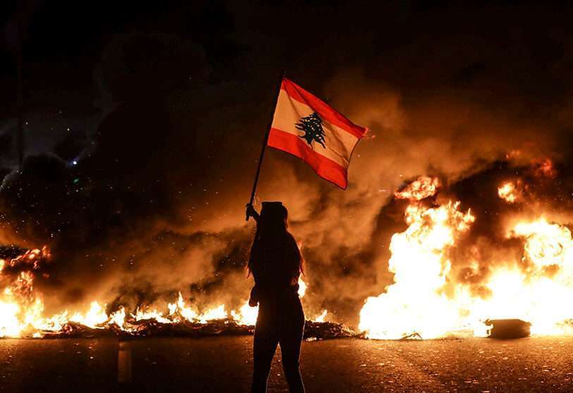Un manifestante antigubernamental ondea una bandera libanesa frente a neumáticos en llamas que bloquean la carretera principal que une la ciudad de Trípoli con Beirut en la ciudad costera de Biblos, al norte de la capital, el 13 de noviembre de 2019
