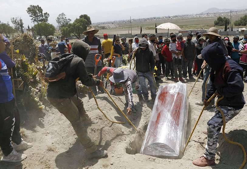 Los trabajadores bajan el ataúd envuelto en plástico de una mujer que murió de la COVID-19 confirmado o sospechoso a una tumba en una nueva sección del Cementerio Municipal de Valle de Chalco