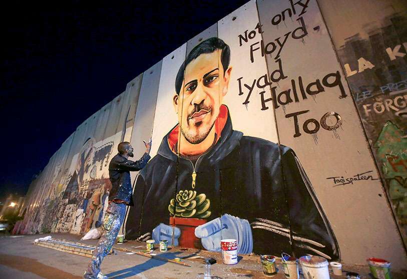 El artista palestino Taqi Spateen junto a su acabado mural de Iyad Hallak, un palestino autista de 32 años muerto a tiros por la policía israelí, en la Cisjordania ocupada, el 14 de junio de 2020