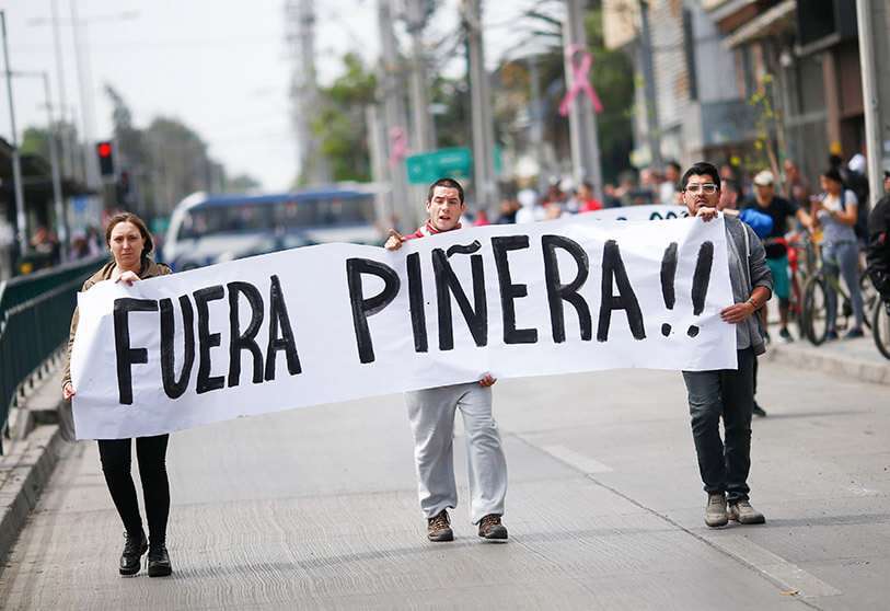 Manifestantes sostienen un letrero que dice “Fuera Piñera” durante los enfrentamientos entre manifestantes y la policía en la Plaza de Maipú en Santiago, el 19 de octubre de 2019