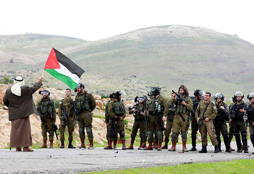 Un manifestante sostiene una bandera palestina frente a las Fuerzas Armadas israelíes durante una protesta contra los asentamientos en Cisjordania
