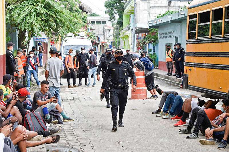 Unos policías pasan por delante de un grupo de migrantes hondureños, que forman parte de una caravana de migrantes con destino a los Estados Unidos, frente a un refugio para migrantes en el municipio de San Marcos (Guatemala), el 3 de octubre de 2020.