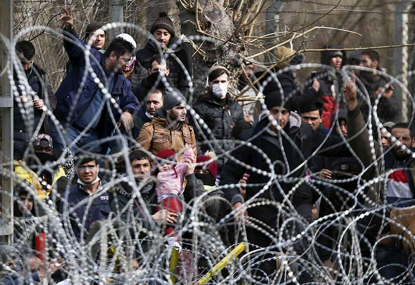 Los migrantes se paran detrás de una valla cerca de la puerta fronteriza de Kastanies en la frontera greco-turca, el lunes 2 de marzo de 2020