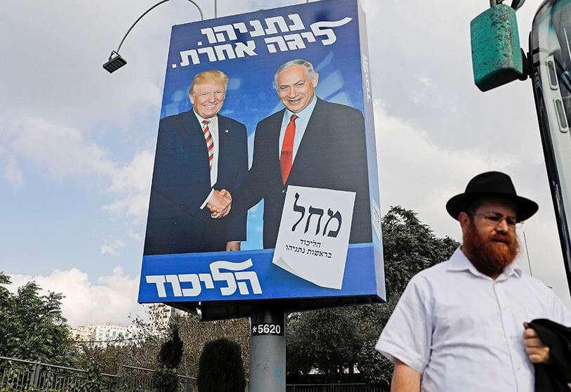 Un hombre israelí pasa por delante de una valla publicitaria electoral del partido Likud, mostrando al presidente de Estados Unidos Donald Trump estrechando la mano del presidente del Likud y del primer ministro Benjamin Netanyahu, en Jerusalén el 16 de septiembre de 2019