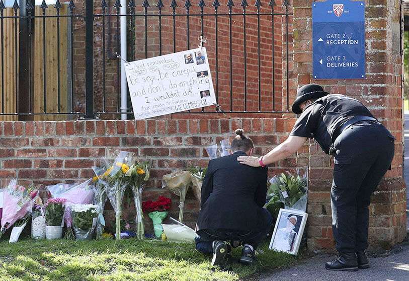 Un oficial de policía consuela a un joven mientras se colocan homenajes florales en la entrada de la Escuela Holt en Wokingham, Inglaterra, en memoria del maestro James Furlong, víctima de un ataque terrorista en la cercana ciudad de Reading, el lunes 22 de junio de 2020