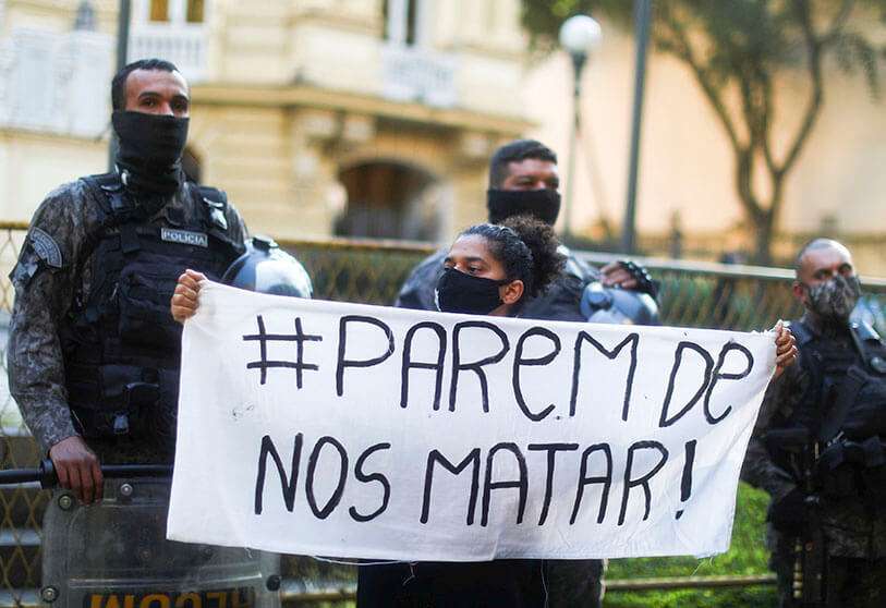 Una mujer con una máscara protectora sostiene una pancarta que dice "Deje de matarnos"