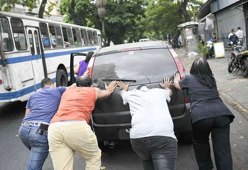 La gente empuja un coche que se quedó sin gasolina a una estación de servicio de la compañía petrolera estatal PDVSA en Caracas, Venezuela, el lunes 25 de mayo de 2020