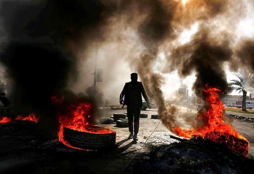 Un hombre camina entre neumáticos quemados durante las continuas protestas antigubernamentales en Najaf, Irak