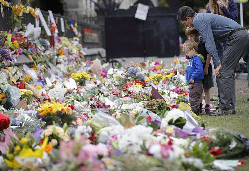 AP/VINCENT THIAN - In this archive photo from 18 March 2019, a family puts flowers on a wall in Christchurch Botanical Garden in New Zealand. 