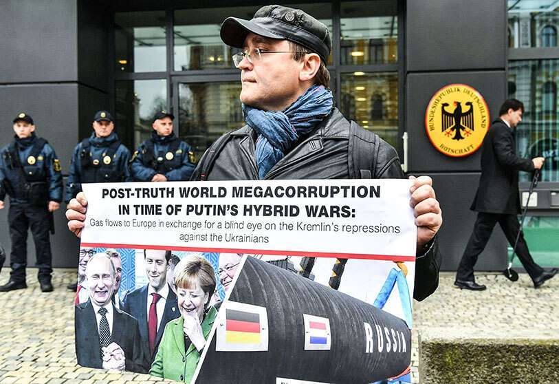 Un hombre sostiene una pancarta que representa al presidente ruso Vladimir Putin y a la canciller alemana Angela Merkel sonriendo, y el gasoducto Nord Stream 2, durante una manifestación frente a la embajada alemana en Kiev, el 11 de abril de 2019 AP/SERGEY SUPINSKY