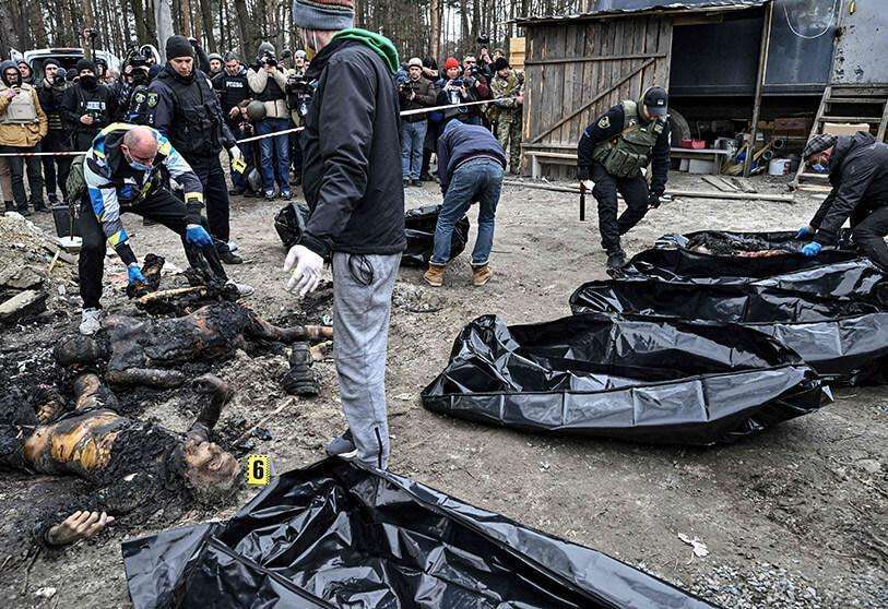 Policías y trabajadores de la ciudad llevan seis cuerpos parcialmente quemados en bolsas para cadáveres mientras los periodistas asisten a la ciudad de Bucha el 5 de abril de 2022, mientras las autoridades ucranianas dicen que se han recuperado más de 400 cuerpos de civiles de la región más amplia de Kiev, muchos de los cuales fueron enterrados en fosas comunes