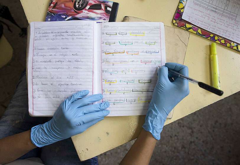 Un profesor que usa guantes quirúrgicos como precaución contra la propagación del nuevo coronavirus, corrige las tareas de un estudiante en la escuela "Fe y Alegría", cerrada a la instrucción en clase debido al cierre del gobierno en Caracas, Venezuela, el martes 12 de mayo de 2020.