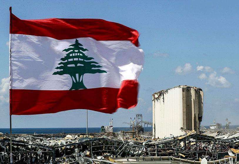 AFP/JOSEPH EID - Una bandera libanesa ondeando a lo largo de un puente cerca del puerto de la capital del Líbano, Beirut, mientras que en el fondo se ven los silos de grano dañados frente al lugar de la explosión