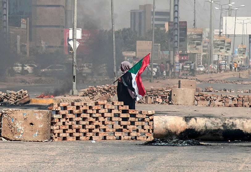 PHOTO/AFP - Un manifestante sudanés con una bandera nacional camina junto a las barricadas instaladas por los manifestantes en una calle de la capital, Jartum, el 26 de octubre de 2021